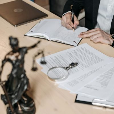 Professional working on documents at desk with legal statue and magnifying glass.